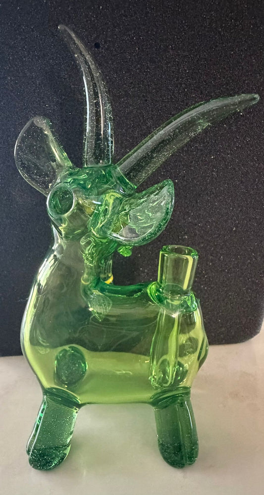 Robertson Glass Green glass goat rig figurine with long horns on a dark background