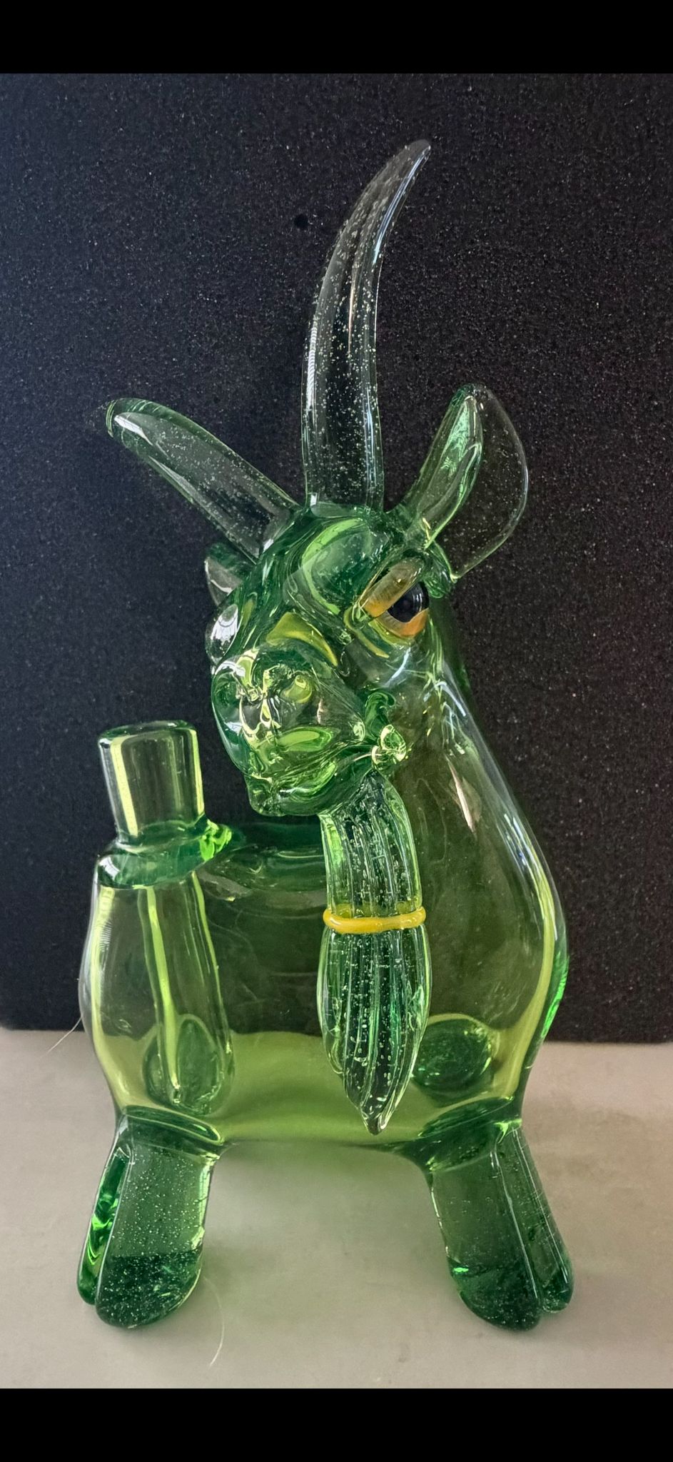 Robertson Glass Green glass goat rig figurine with long horns on a dark background