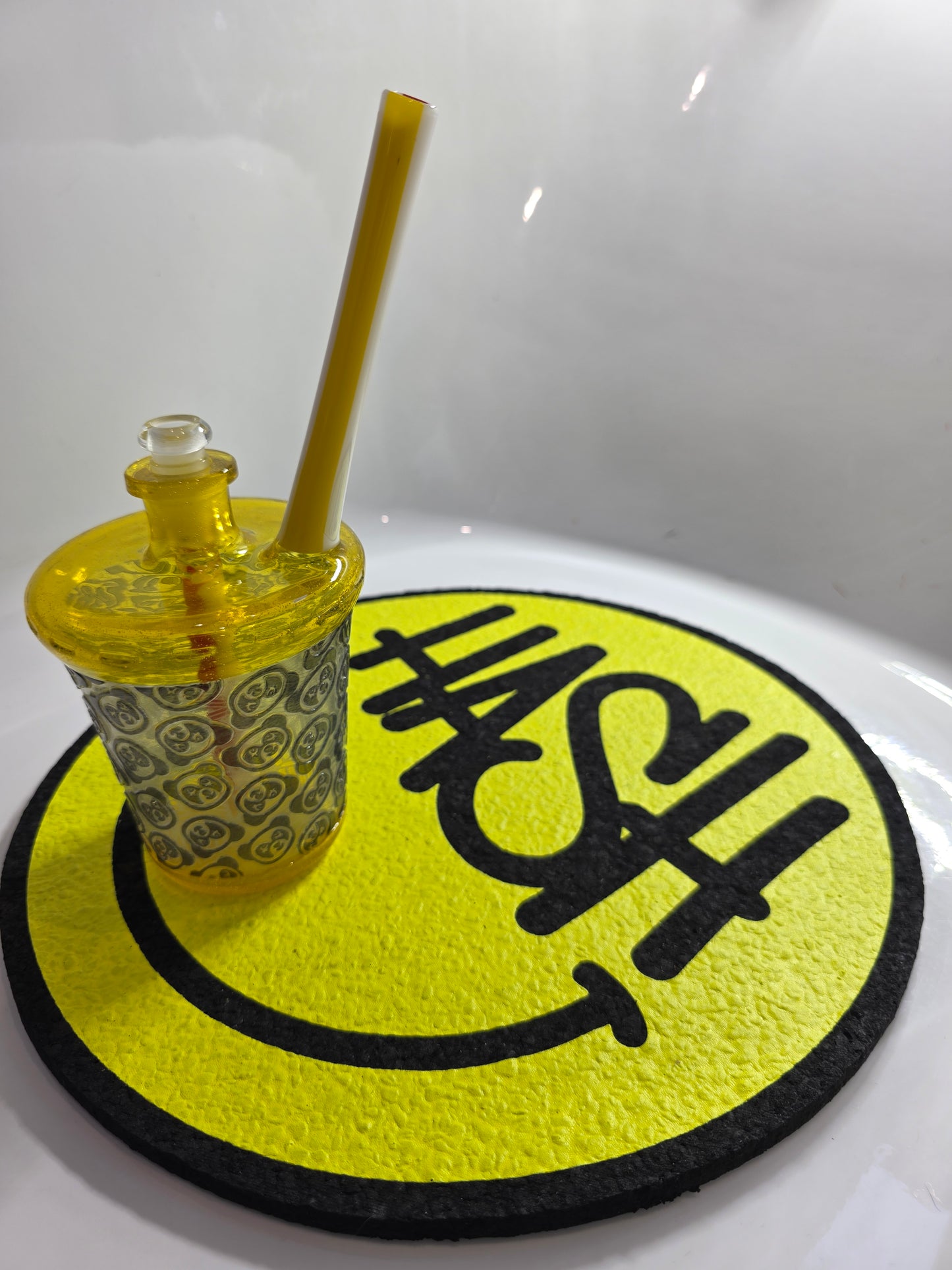 Slop Glass x Disk Glass Yellow glass rig cup with patterned base, red straw, and decorative lid on a reflective surface.