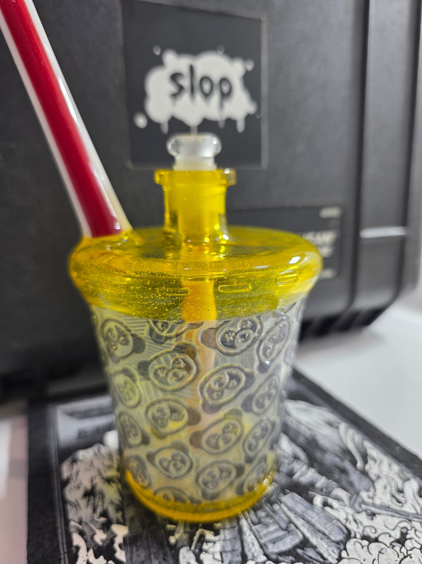 Slop Glass x Disk Glass Yellow glass rig cup with patterned base, red straw, and decorative lid on a reflective surface.