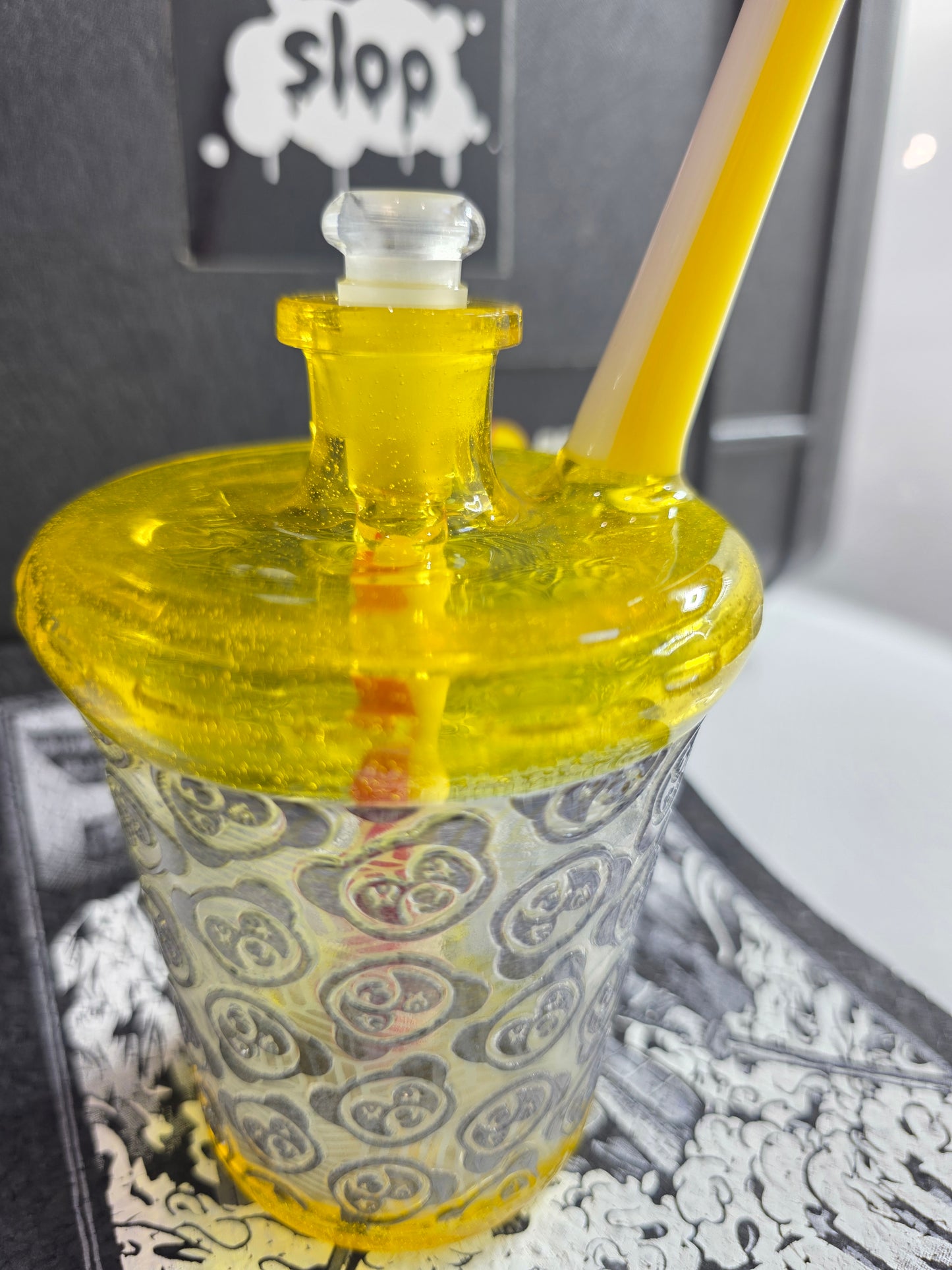 Slop Glass x Disk Glass Yellow glass rig cup with patterned base, red straw, and decorative lid on a reflective surface.