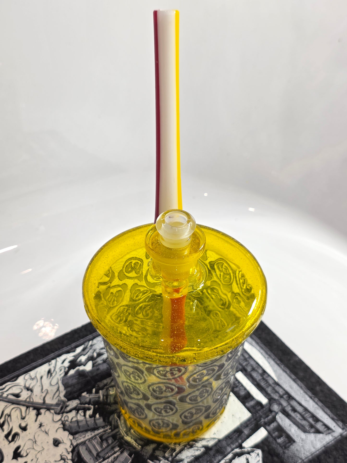 Slop Glass x Disk Glass Yellow glass rig cup with patterned base, red straw, and decorative lid on a reflective surface.