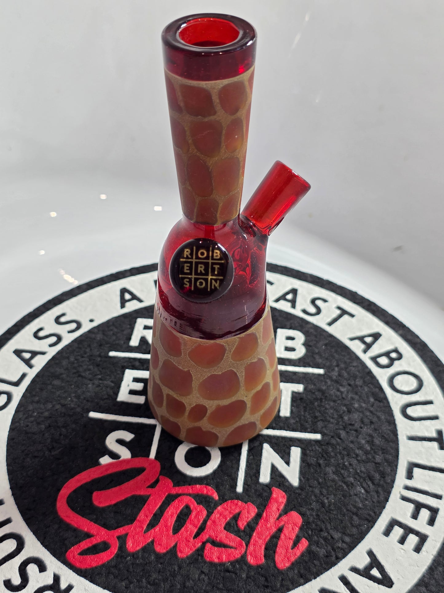 Robertson Glass Rig .Glass rig with red interior on a white surface with 'Stash' branding.