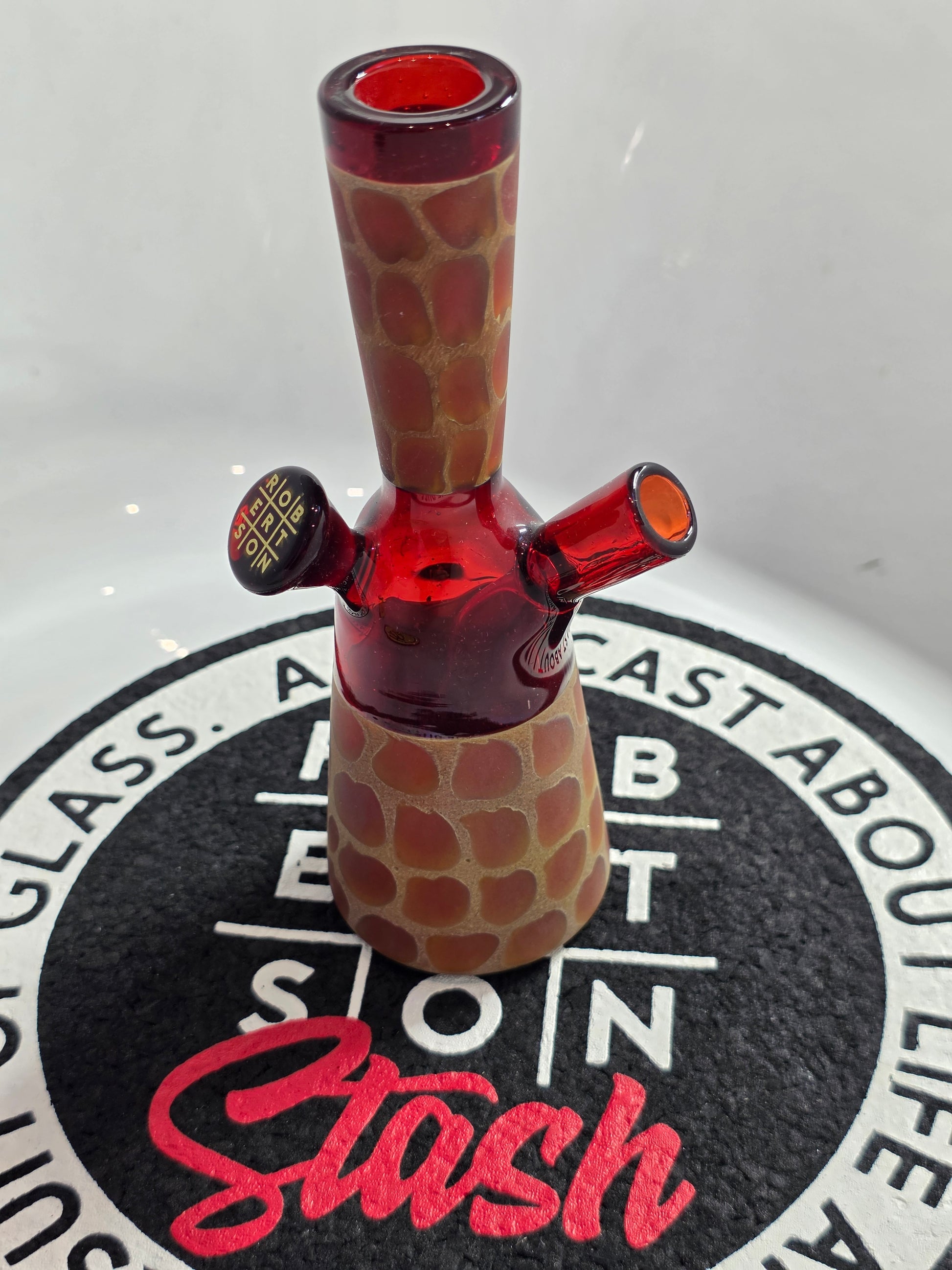 Robertson Glass Rig .Glass rig with red interior on a white surface with 'Stash' branding.