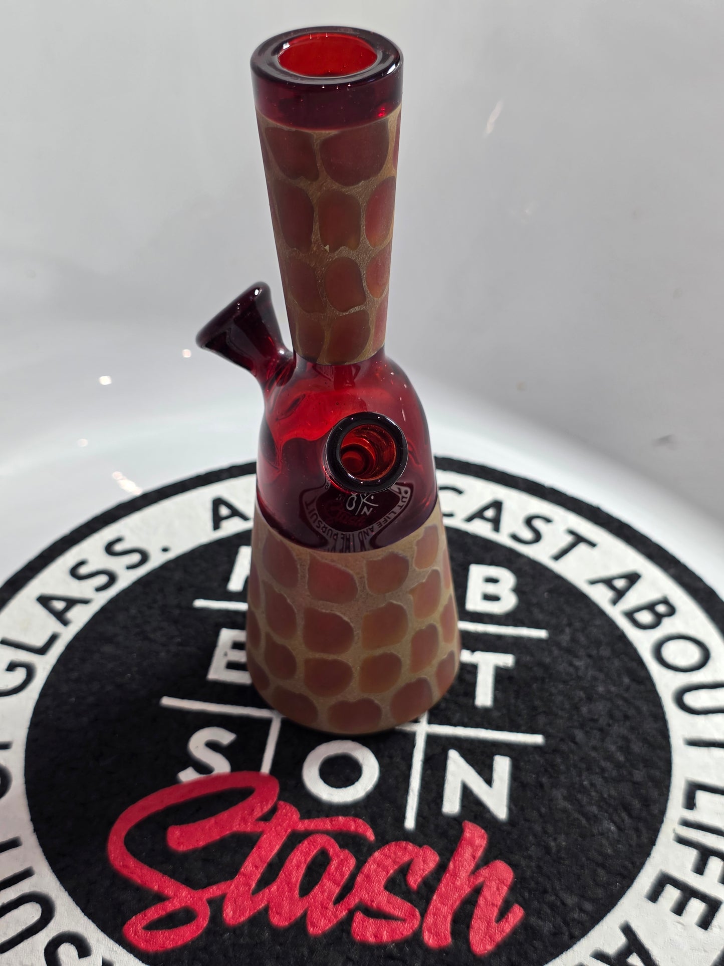 Robertson Glass Rig .Glass rig with red interior on a white surface with 'Stash' branding.