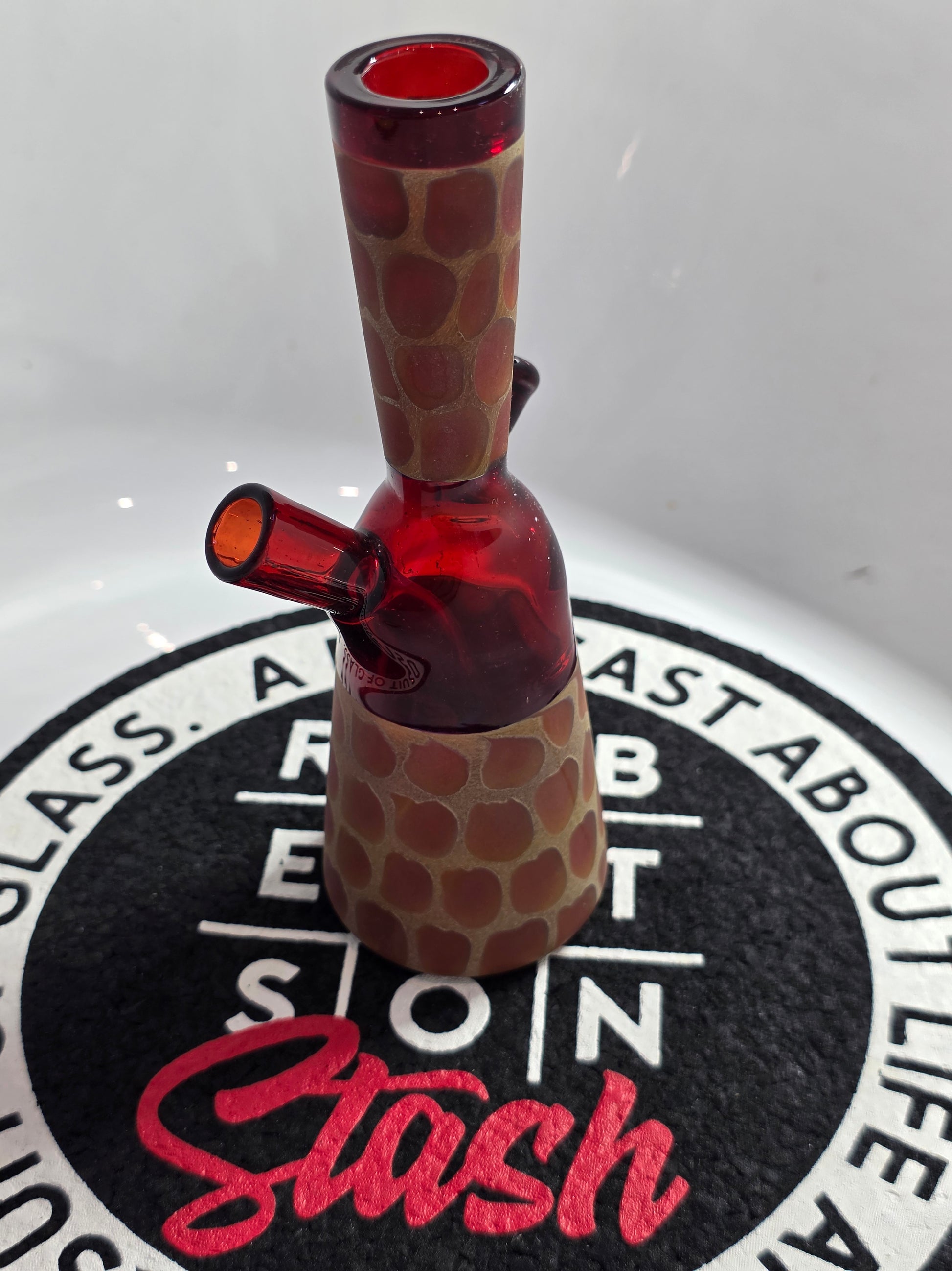 Robertson Glass Rig .Glass rig with red interior on a white surface with 'Stash' branding.