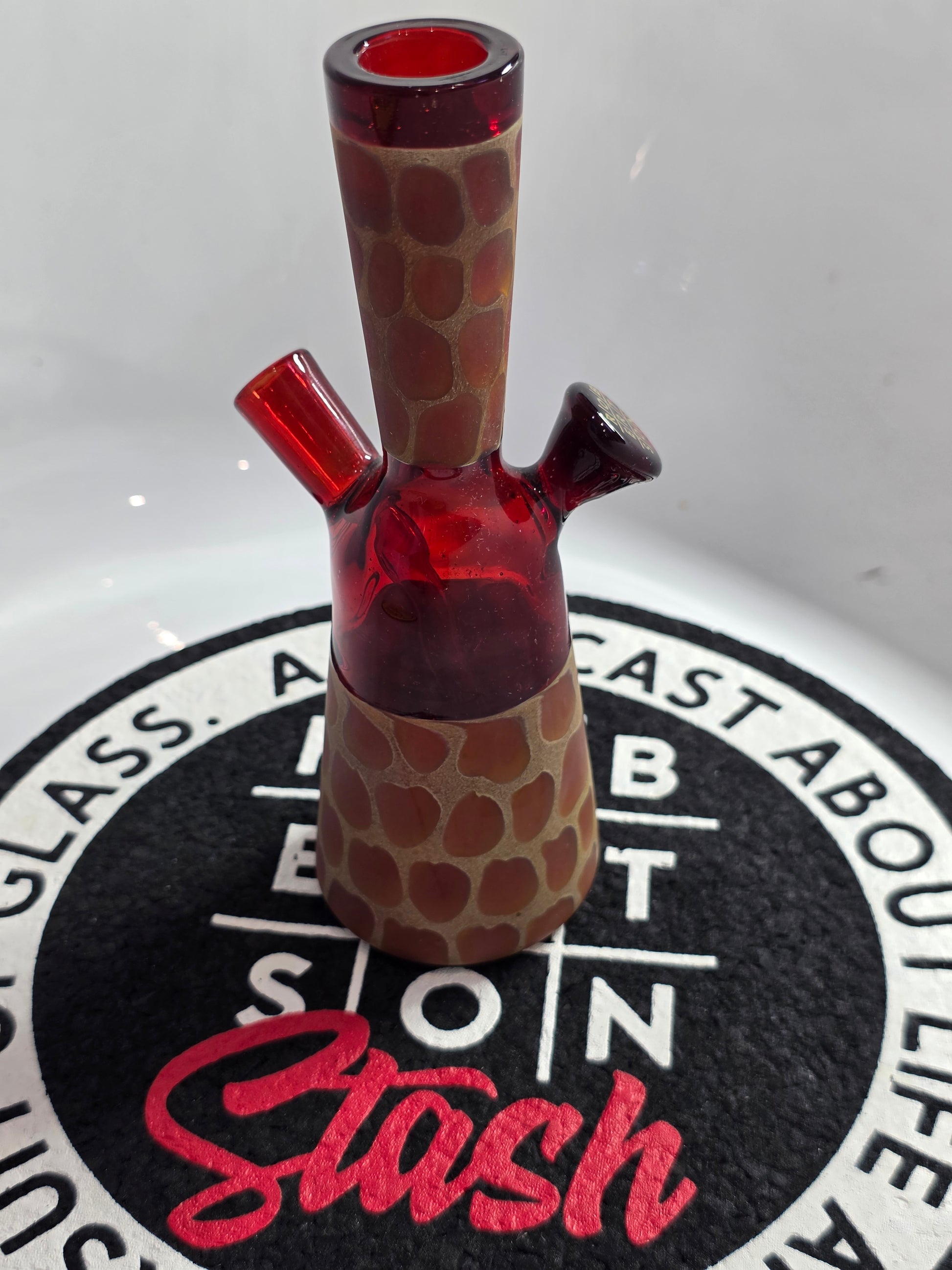 Robertson Glass Rig .Glass rig with red interior on a white surface with 'Stash' branding.