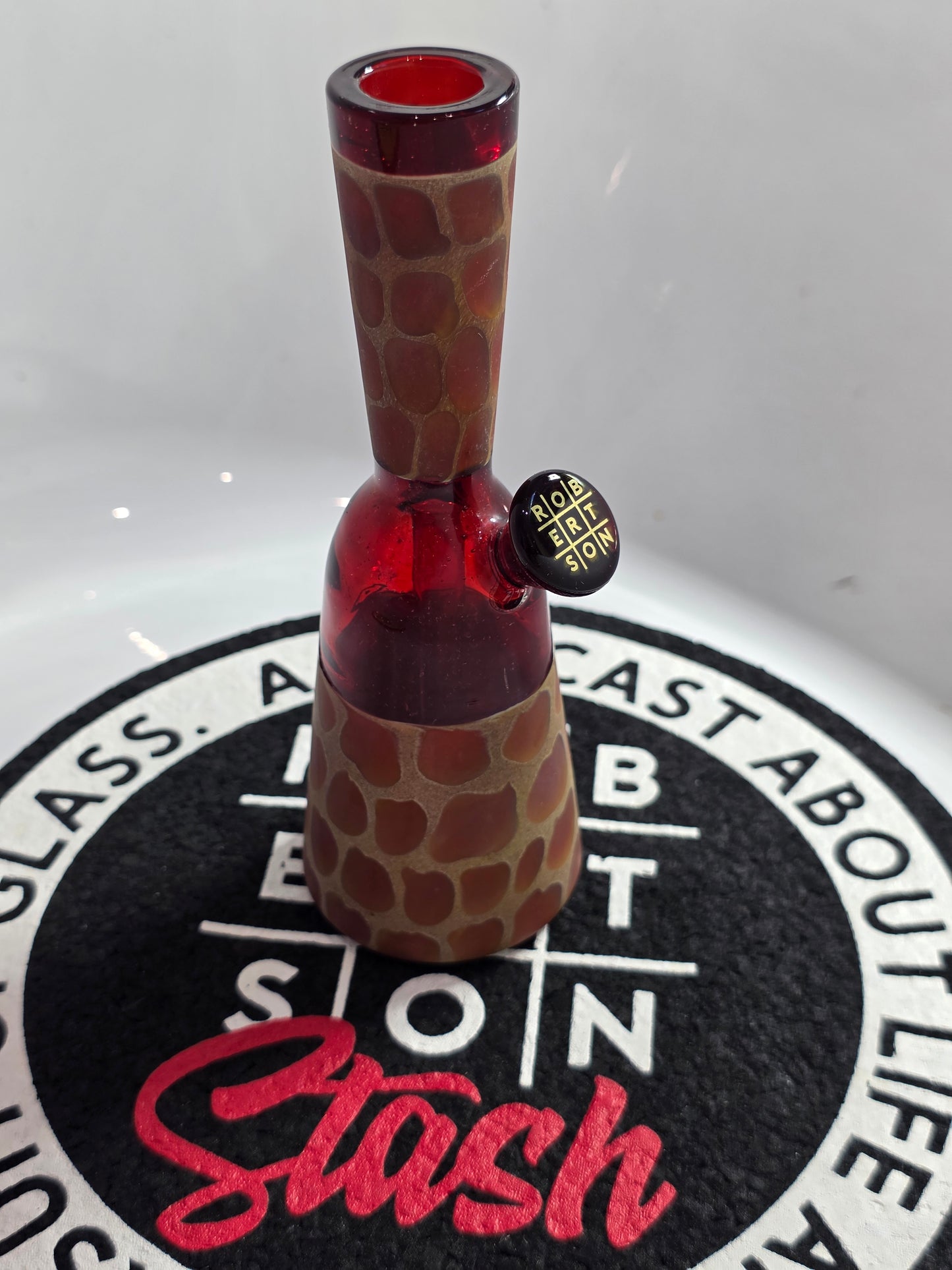 Robertson Glass Rig .Glass rig with red interior on a white surface with 'Stash' branding.