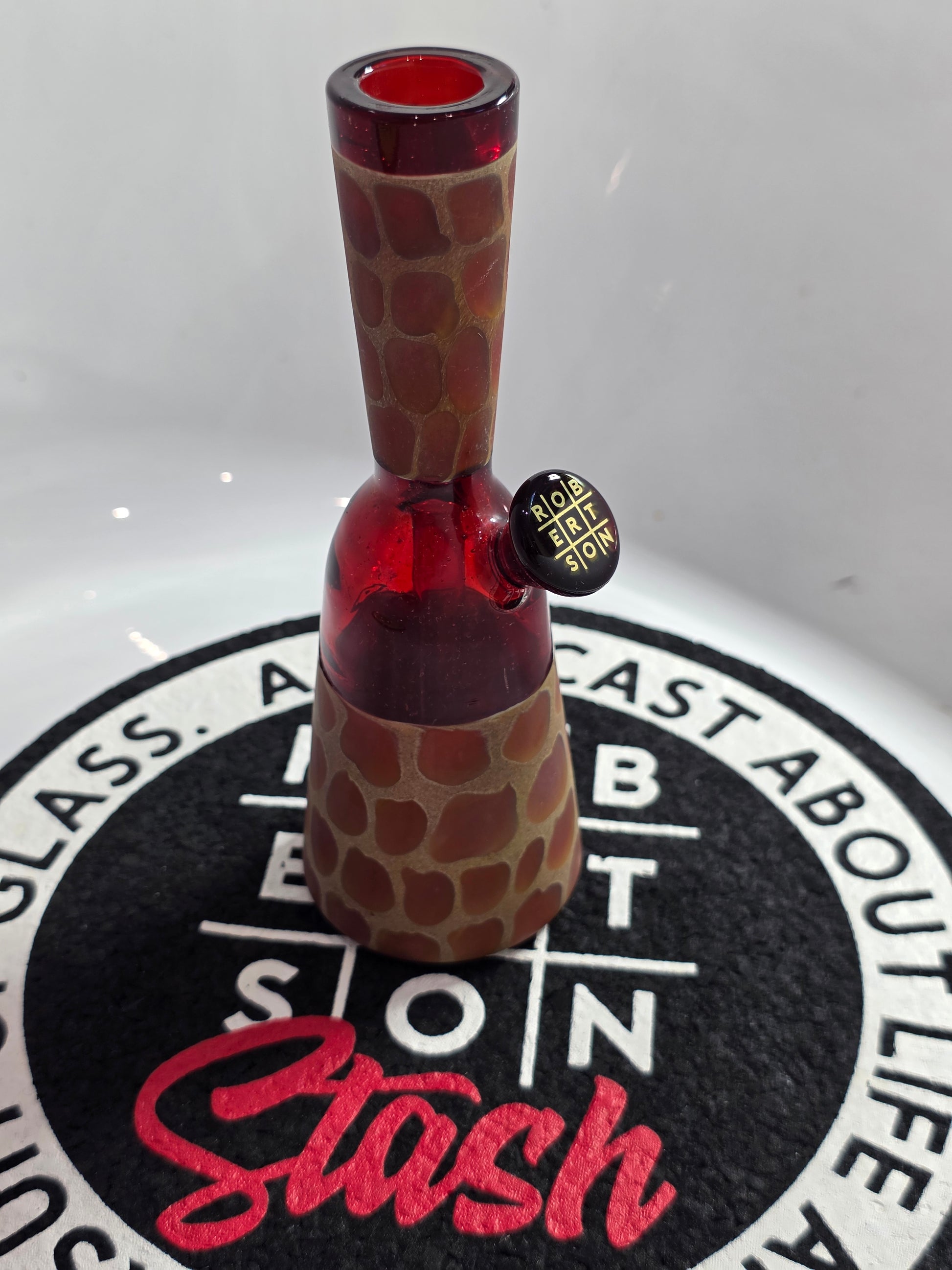 Robertson Glass Rig .Glass rig with red interior on a white surface with 'Stash' branding.