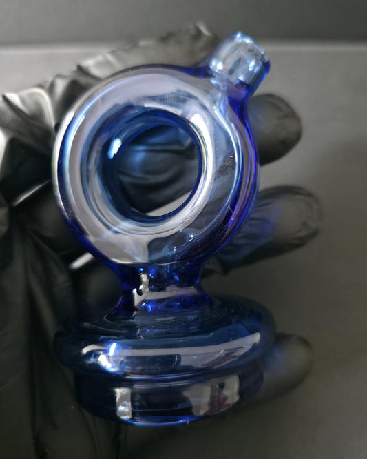 Blue glass smoking accessory held by a gloved hand on a reflective surface