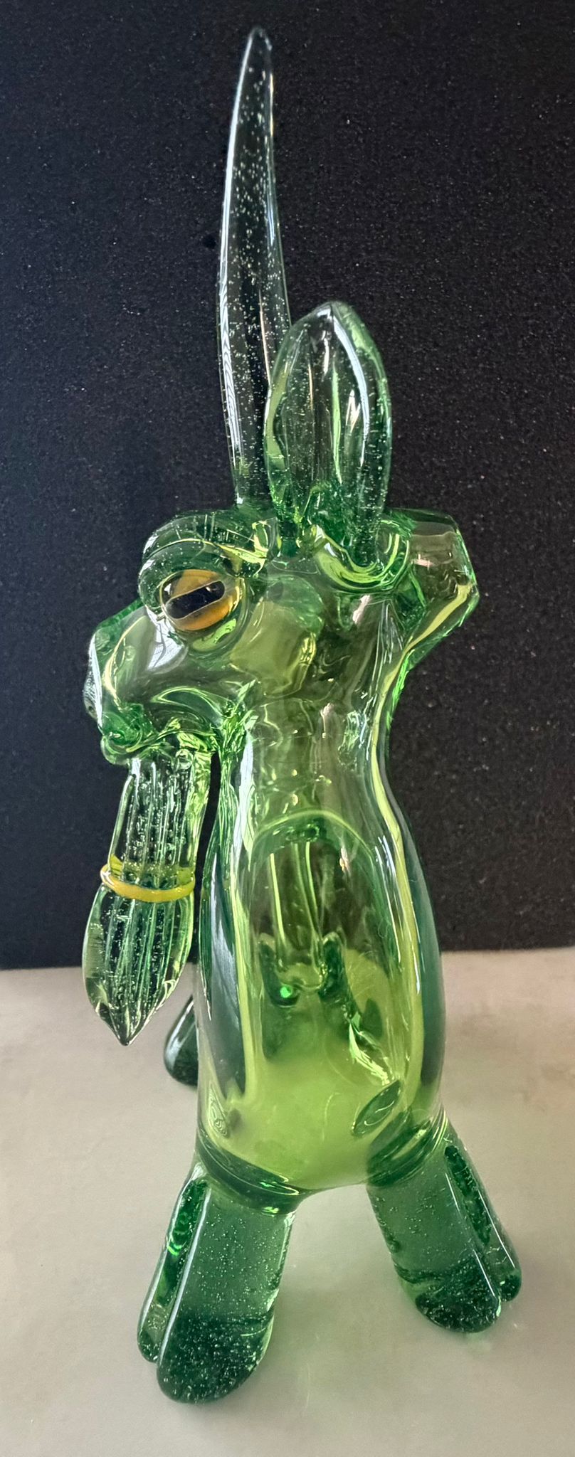 Robertson Glass Green glass goat rig figurine with long horns on a dark background