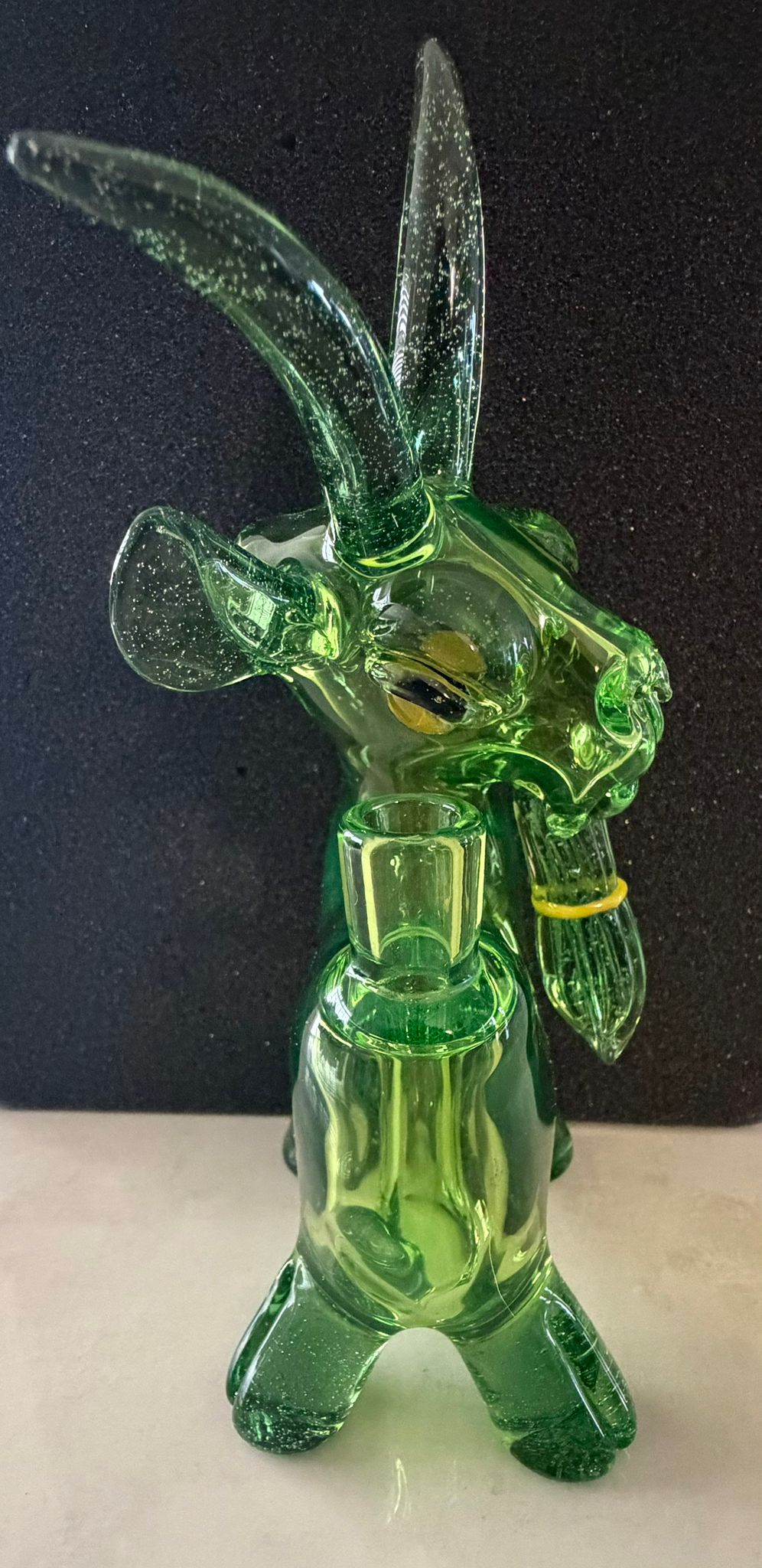 Robertson Glass Green glass goat rig figurine with long horns on a dark background