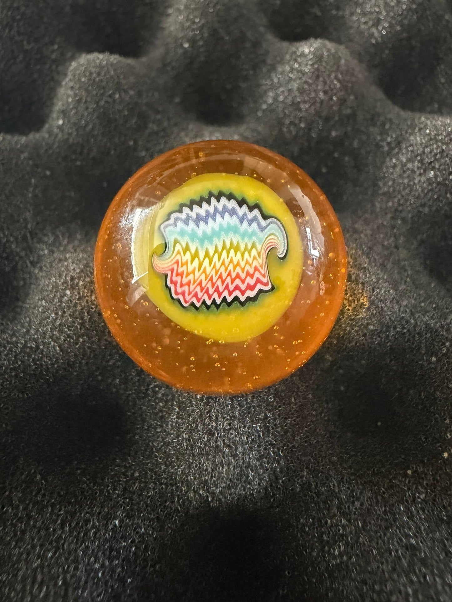 Round amber-colored marble with a colorful design on a black textured background