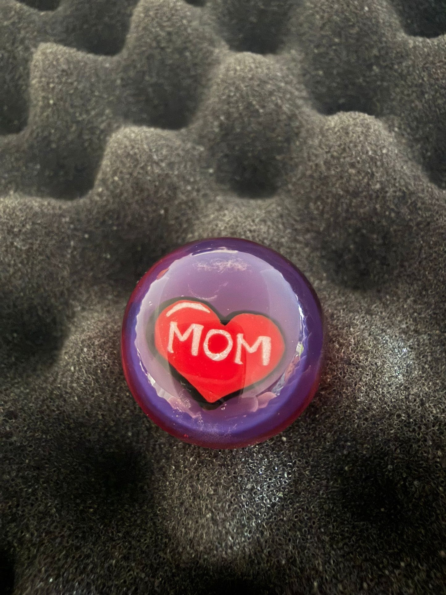 Marble with a red heart and 'MOM' text on a textured black surface