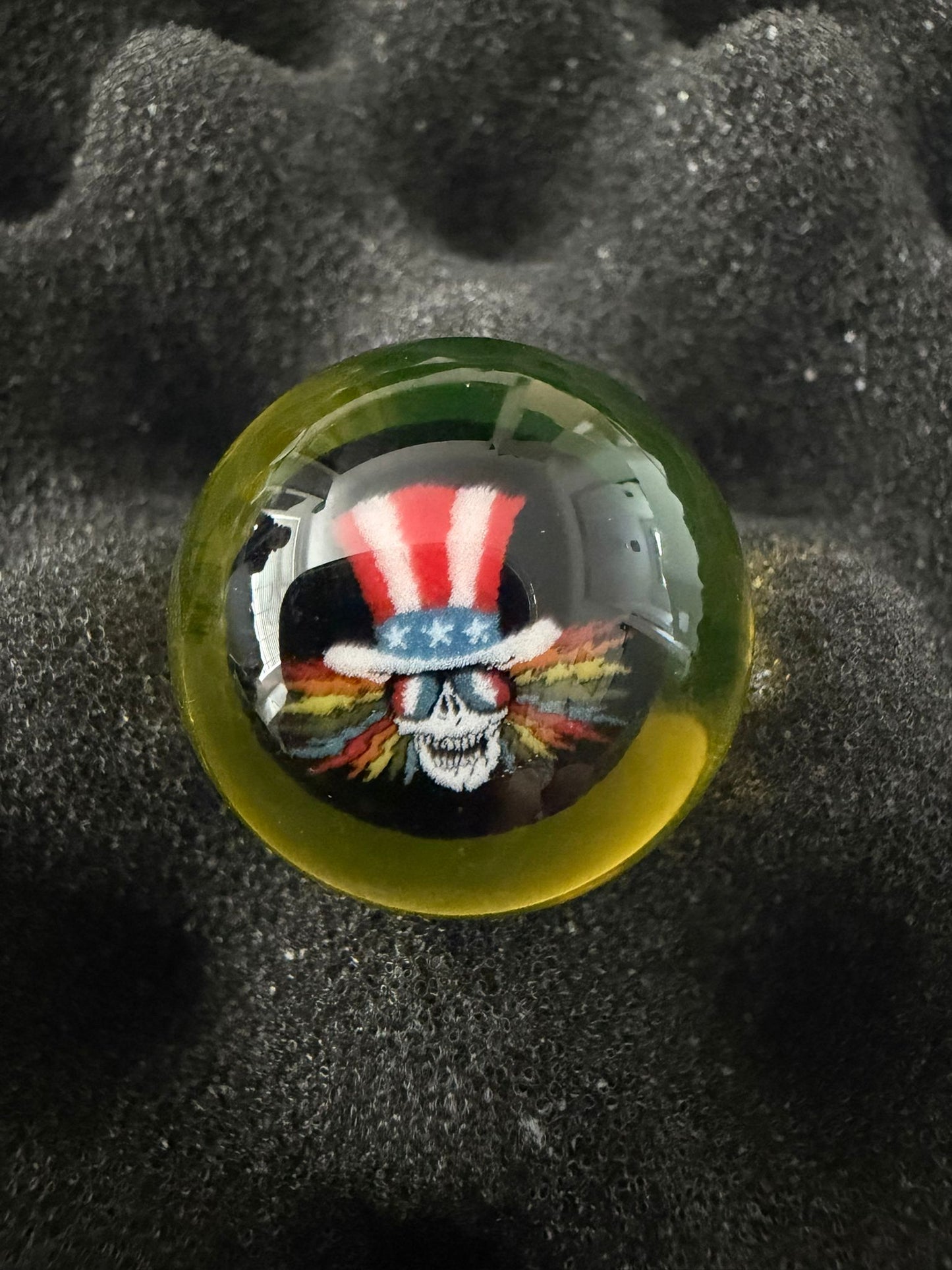 Glass marble with a colorful skull design and American flag hat on a textured black surface