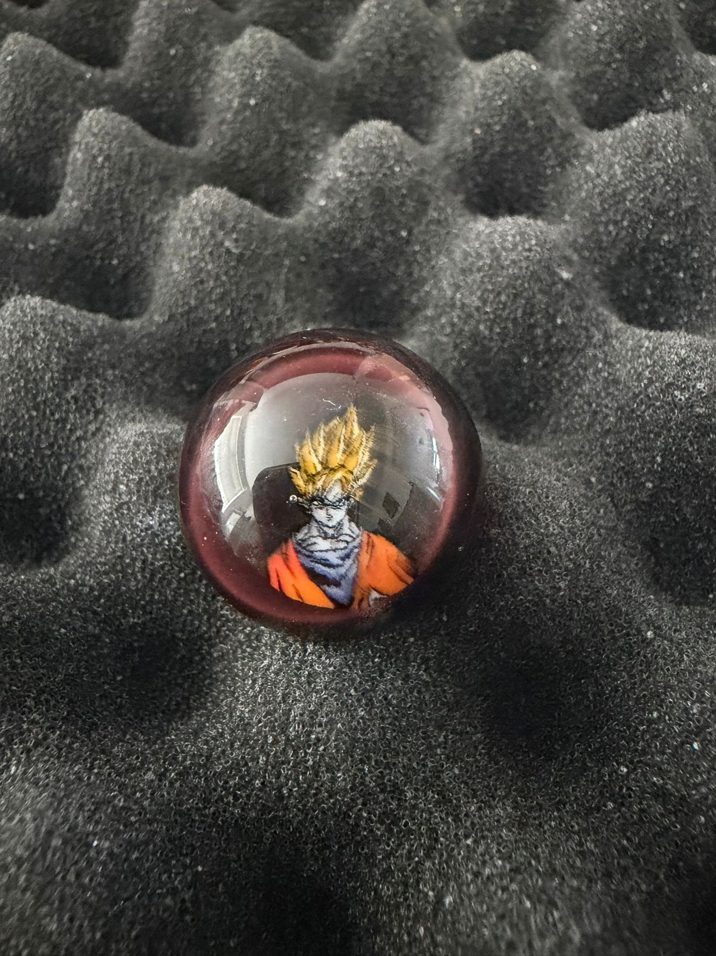 Round glass marble with a character design on a textured black surface