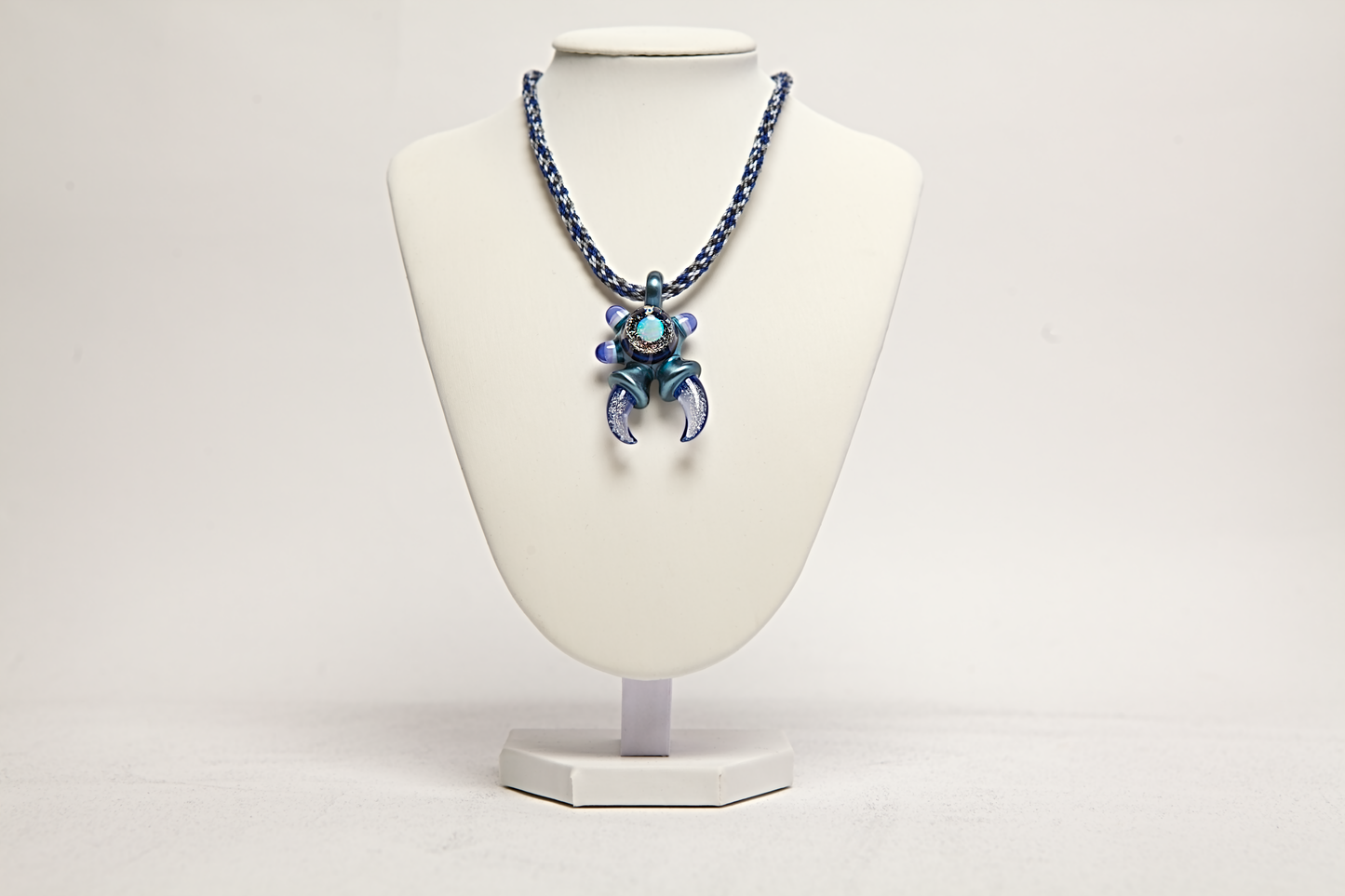 Necklace with a blue and silver pendant on a white mannequin bust against a white background