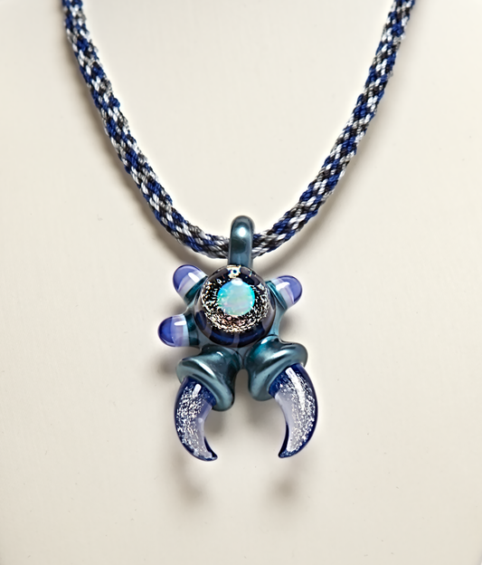 Blue and silver crab-shaped pendant on a braided cord against a light background